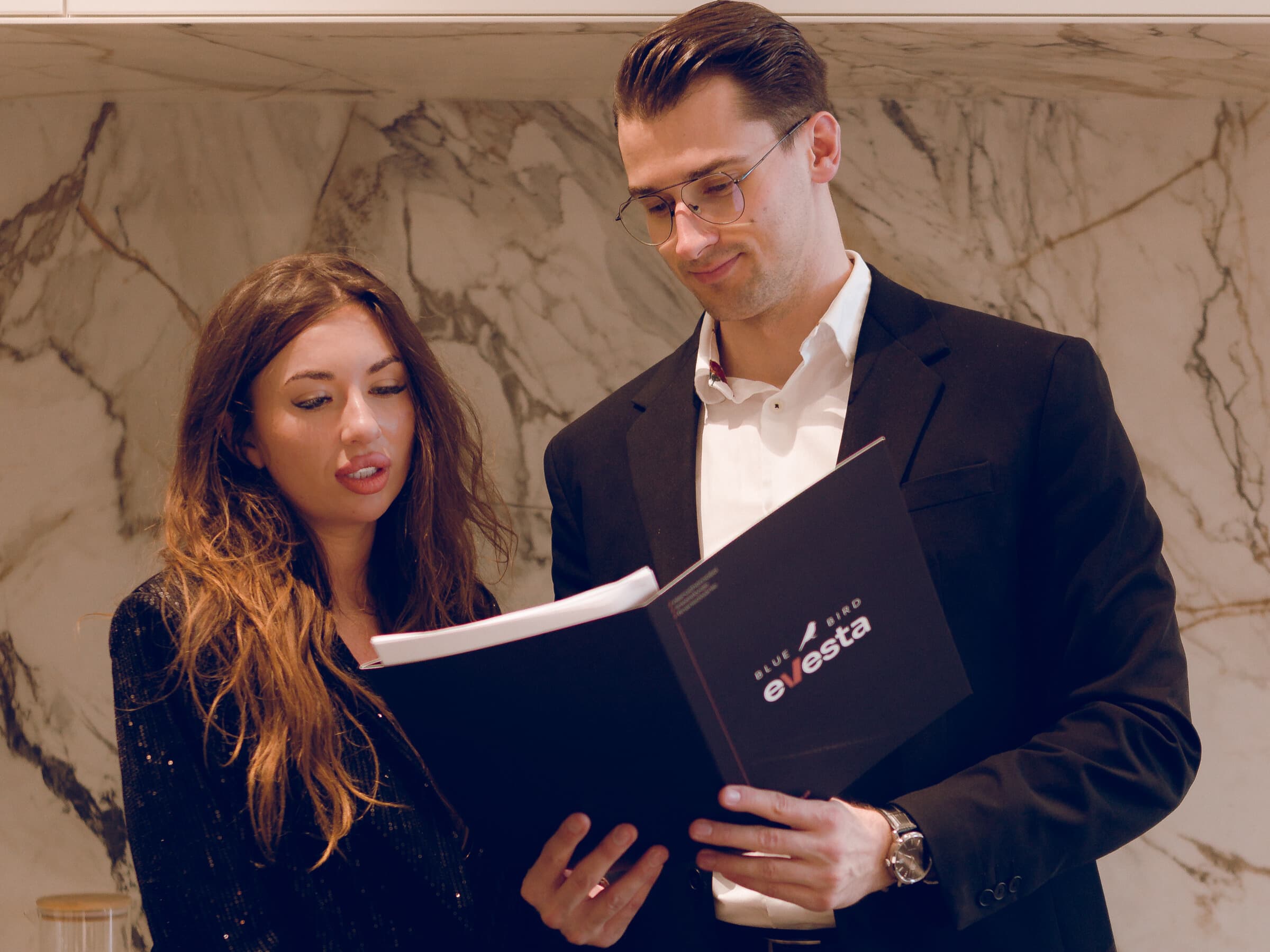 A woman and a man jointly reviewing documents in a binder.