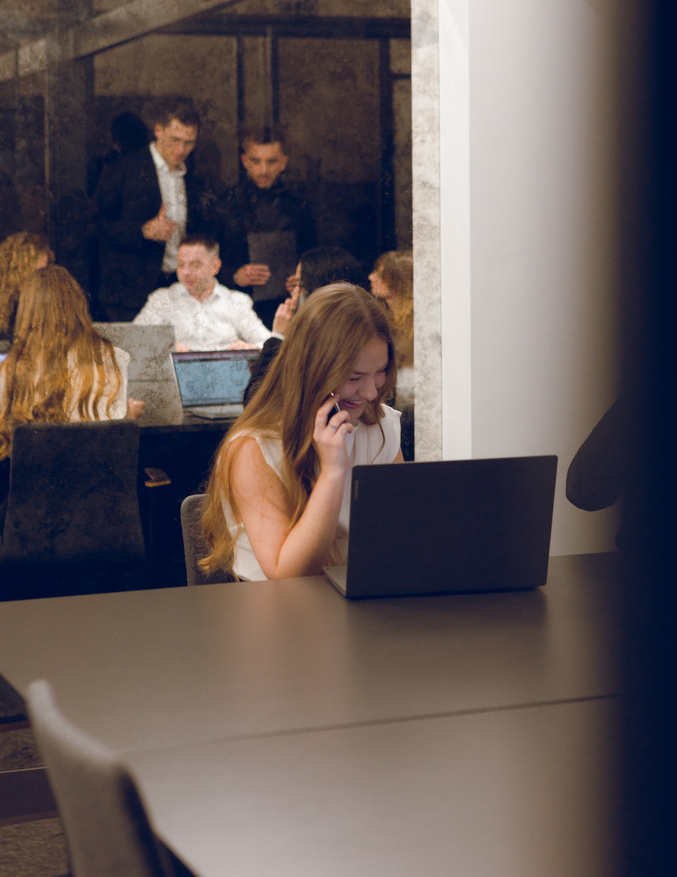 Kobieta rozmawia przez telefon i pracuje na laptopie w ruchliwym biurze.