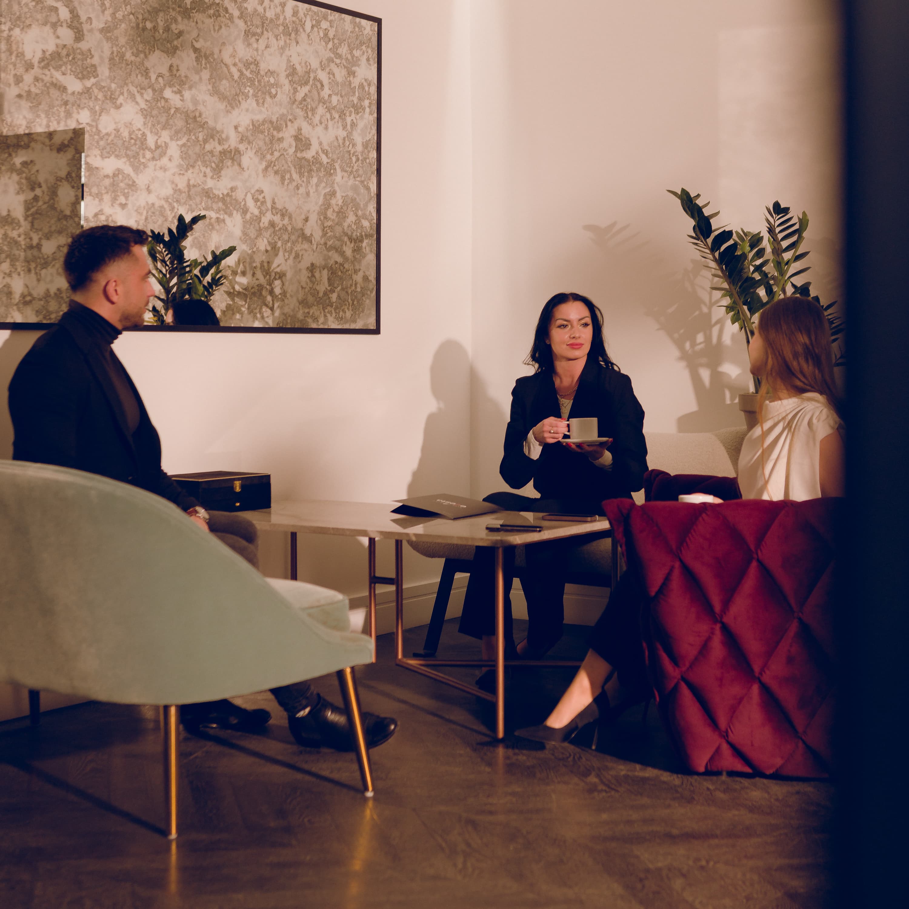 Three people having a conversation sitting in armchairs at a coffee table.